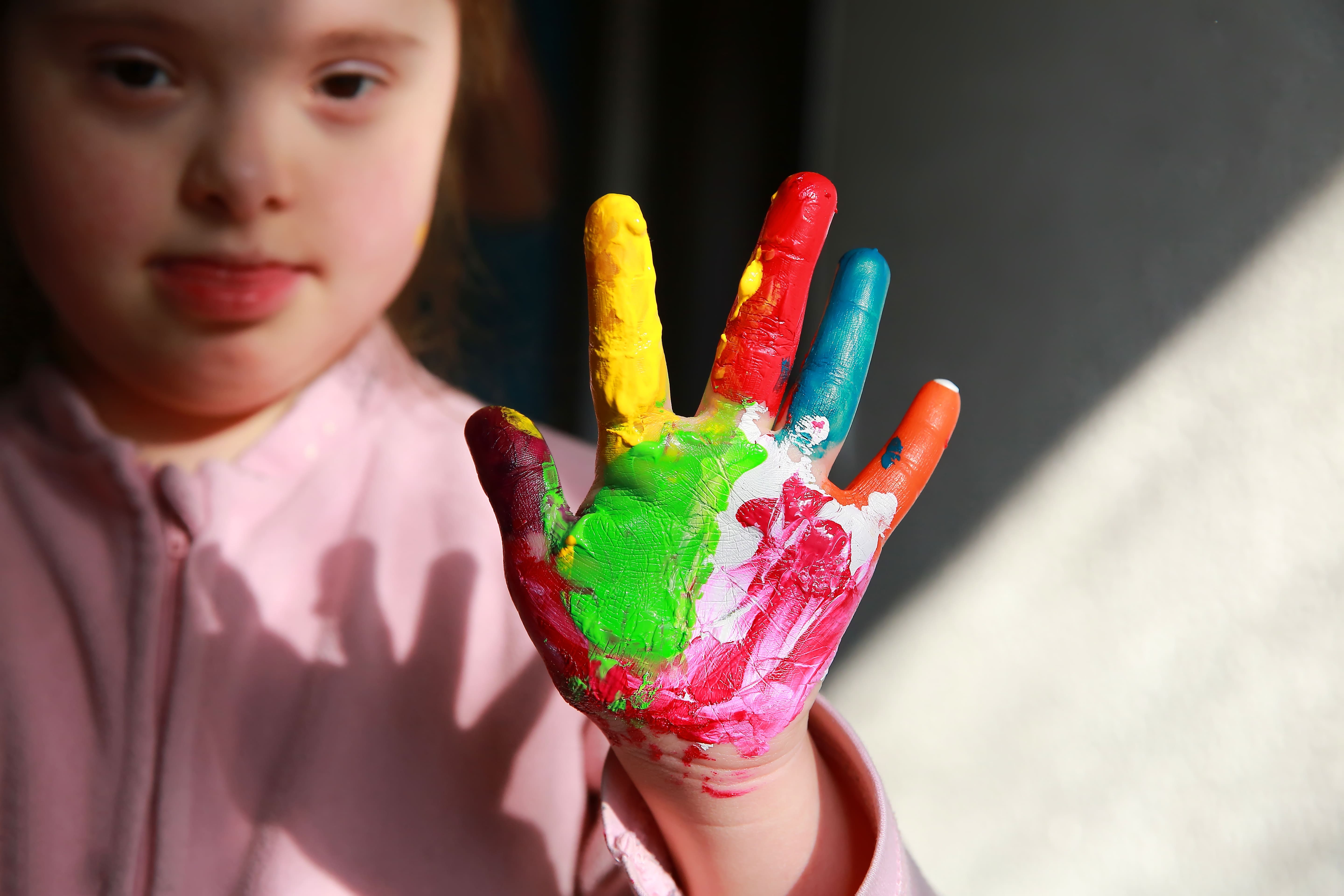 Enfant ayant des besoins spécifiques tendant une main peinte de plusieurs couleurs