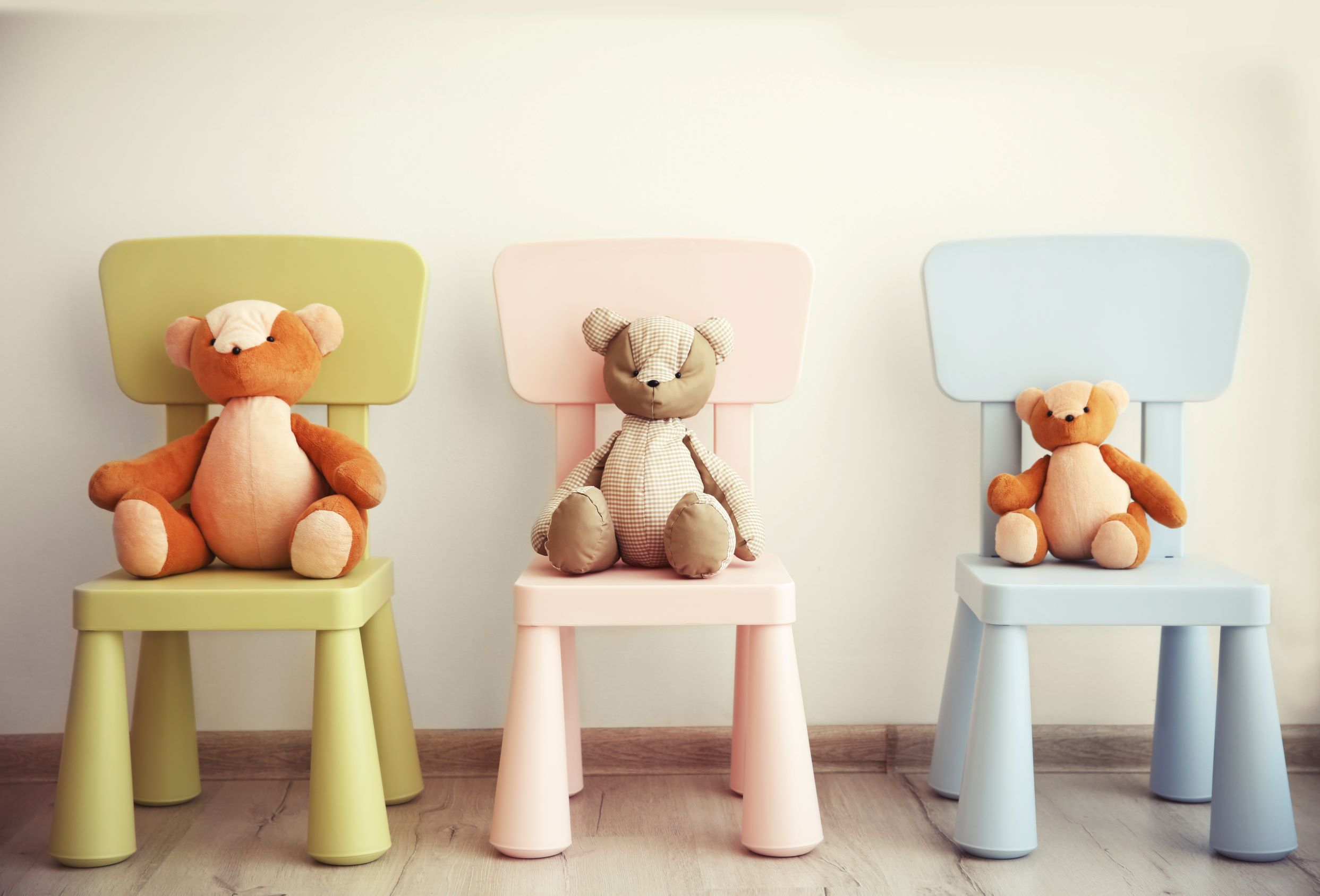 Trois chaises pour enfant de couleurs différentes, chacune occupée par une peluche